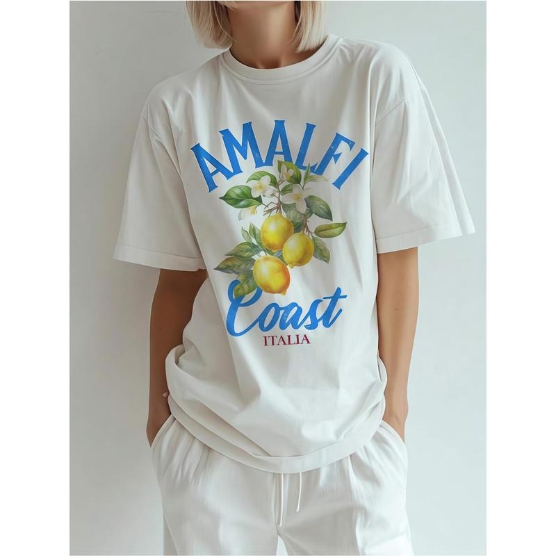 A Female Model in a T-Shirt Featuring 'AMALFI Coast' and 'ITALIA' with a Lemon Pattern, Hands in Pockets, Evoking a Sense...